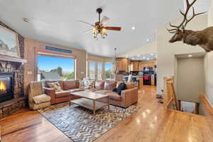 Living room featuring lofted ceiling, light wood-style floors, a textured ceiling, a stone fireplace, and recessed lighting