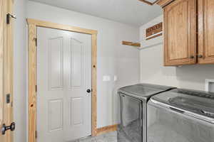 Washroom featuring a textured ceiling, cabinet space, washer and clothes dryer, and light tile patterned flooring