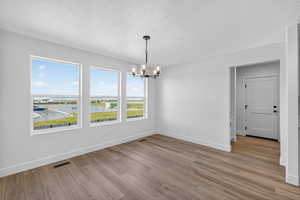 Unfurnished dining area with a textured ceiling, a chandelier, and light wood-type flooring