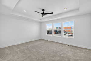 Spare room with a tray ceiling, light carpet, ceiling fan, and recessed lighting
