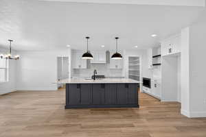 Kitchen featuring white cabinets, a kitchen island with sink, backsplash, hanging light fixtures, and recessed lighting