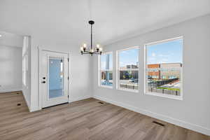 Unfurnished dining area with a chandelier, light wood-style floors, and a textured ceiling