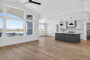 Kitchen featuring white cabinets, hanging light fixtures, an island with sink, backsplash, and light wood finished floors