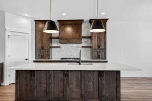 Kitchen featuring dark brown cabinets, backsplash, an island with sink, open shelves, and hanging light fixtures