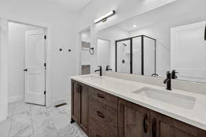 Full bathroom featuring a shower stall, double vanity, and light marble finish flooring