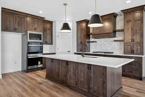 Kitchen with decorative backsplash, dark brown cabinets, hanging light fixtures, open shelves, and recessed lighting