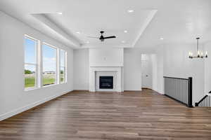 Unfurnished living room featuring a raised ceiling, wood finished floors, recessed lighting, and a glass covered fireplace