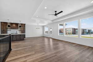 Unfurnished living room featuring dark wood finished floors, recessed lighting, a chandelier, ceiling fan, and a raised ceiling