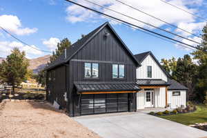 Modern inspired farmhouse featuring board and batten siding, a standing seam roof, driveway, a garage, and a metal roof
