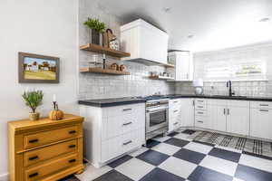 Kitchen with dark countertops, white cabinetry, dark flooring, and gas range