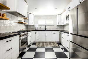 Kitchen featuring stainless steel appliances, dark floors, open shelves, white cabinets, and decorative backsplash