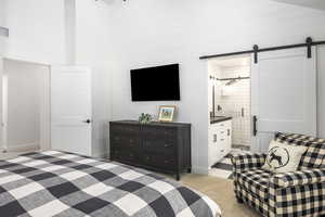 Bedroom with a barn door, a towering ceiling, light carpet, and ensuite bathroom
