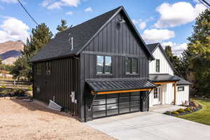 View of front of house with board and batten siding, a shingled roof, driveway, an attached garage, and a standing seam roof