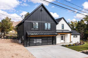 Modern inspired farmhouse featuring a standing seam roof, board and batten siding, a garage, a metal roof, and driveway