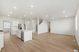 Kitchen featuring a kitchen island with sink, light wood finished floors, white cabinetry, appliances with stainless steel finishes, and recessed lighting