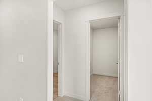 Hallway featuring light colored carpet and baseboards