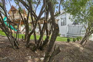View of green lawn featuring a trampoline and a playground