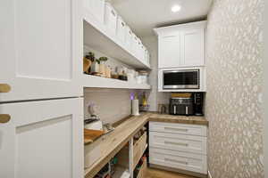 Kitchen featuring white cabinetry, open shelves, backsplash, stainless steel microwave, and wooden counters