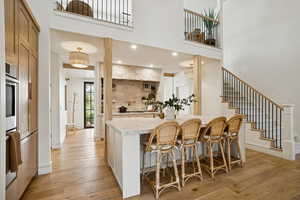 Kitchen featuring light wood finished floors, a towering ceiling, a breakfast bar, stainless steel double oven, and light stone counters