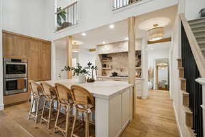 Kitchen with light wood finished floors, a breakfast bar, stainless steel double oven, an island with sink, and a high ceiling