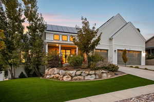 Modern farmhouse style home featuring board and batten siding, a yard, a porch, concrete driveway, and roof mounted solar panels
