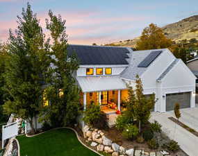 Modern farmhouse featuring a porch, driveway, board and batten siding, roof mounted solar panels, and a standing seam roof