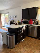 Kitchen featuring dark cabinets, light countertops, appliances with stainless steel finishes, a peninsula, and a textured ceiling