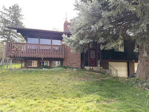 Rear view of property featuring a chimney, brick siding, a yard, a deck, and a garage