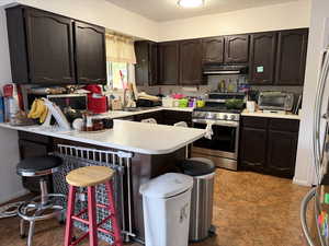 Kitchen with dark brown cabinets, a textured ceiling, a kitchen breakfast bar, appliances with stainless steel finishes, and light countertops