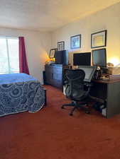 Bedroom with a textured ceiling, carpet floors, an office area, and a textured wall