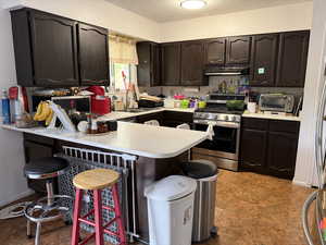 Kitchen featuring dark brown cabinets, a kitchen breakfast bar, a textured ceiling, stainless steel appliances, and light countertops