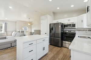 Kitchen featuring lofted ceiling, white cabinetry, stainless steel appliances, open floor plan, and recessed lighting