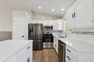 Kitchen with stainless steel appliances, white cabinets, vaulted ceiling, light stone counters, and light wood-style flooring