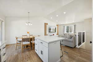 Kitchen with vaulted ceiling, hanging light fixtures, light countertops, open floor plan, and white cabinets