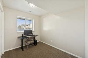 Home office with dark colored carpet and a textured ceiling