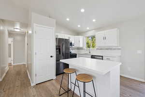 Kitchen featuring lofted ceiling, appliances with stainless steel finishes, white cabinetry, tasteful backsplash, and a breakfast bar