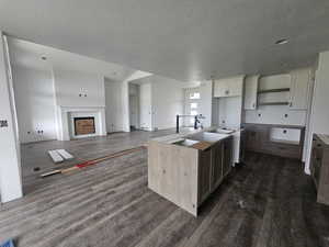 Kitchen featuring dark wood-style flooring, a textured ceiling, a center island, a fireplace, and open floor plan