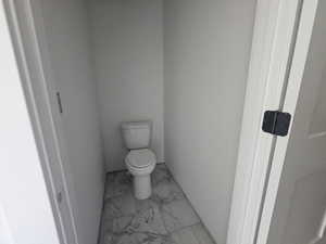 Bathroom featuring toilet and light marble finish flooring