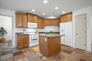 Kitchen featuring white appliances, a center island, brown cabinetry, and recessed lighting