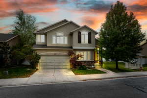 Traditional-style home featuring a front lawn, stucco siding, concrete driveway, an attached garage, and stone siding