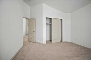 Unfurnished bedroom featuring light colored carpet, a closet, and high vaulted ceiling