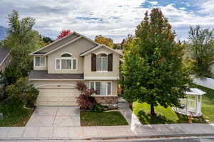 View of front facade featuring stucco siding, concrete driveway, stone siding, a garage, and a front yard