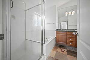 Full bath with a jetted tub, vanity, a shower stall, lofted ceiling, and stone tile flooring