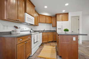 Kitchen featuring white appliances, recessed lighting, brown cabinets, and a center island