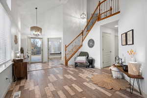 Foyer featuring high vaulted ceiling, a chandelier, hardwood / wood-style flooring, and stairs