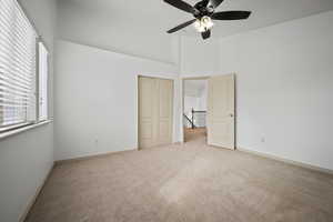 Unfurnished bedroom featuring carpet, ceiling fan, a closet, and a towering ceiling