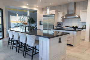 Kitchen featuring white cabinets, wall chimney exhaust hood, tasteful backsplash, stainless steel appliances, and recessed lighting