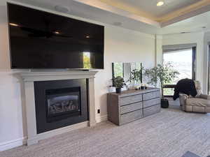 Living room featuring carpet flooring, a glass covered fireplace, recessed lighting, a raised ceiling, and ceiling fan