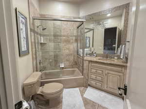 Full bathroom with bath / shower combo with glass door, vanity, light tile patterned floors, and ensuite bath