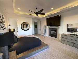 Bedroom with a tray ceiling, recessed lighting, light colored carpet, a fireplace, and ceiling fan